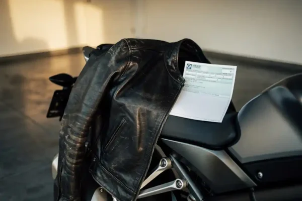Veste de moto en cuir usé posée sur une selle moderne avec un document d'assurance froissé, éclairage doré dans un garage belge.