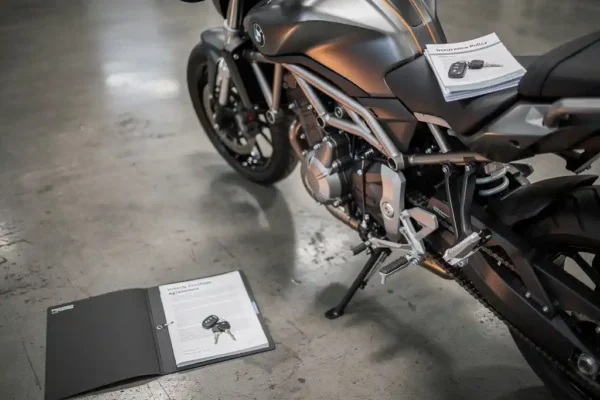 Moto neuve garée en concession avec contrat d'achat, clés et documents d'assurance posés sur la selle, éclairage showroom.