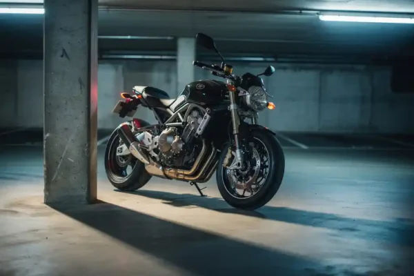 Moto chromée garée dans un parking souterrain sombre, éclairée par une lumière fluorescente bleutée avec ombres de pilier en béton.