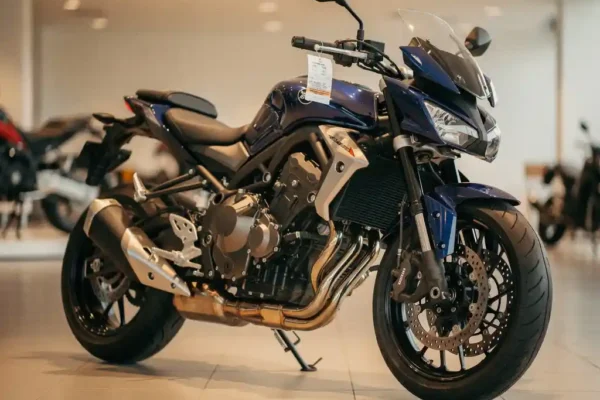Moto neuve bleu marine et argent exposée en concession, étiquette de prix visible sur le guidon, éclairage chaud soulignant les courbes chromées.