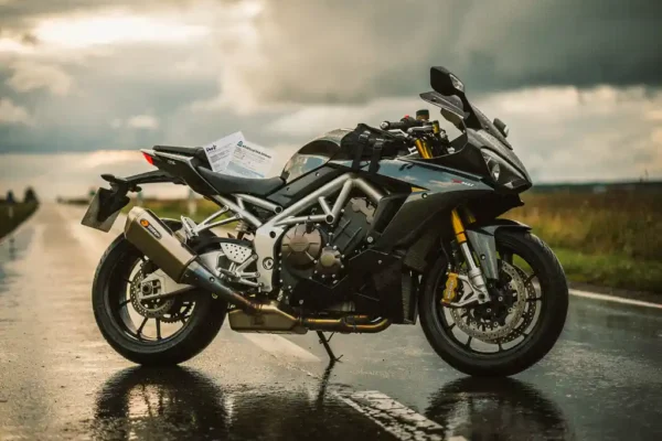 Moto sportive garée sur une route belge mouillée sous un ciel nuageux, documents d'assurance glissés sous la sangle du siège.