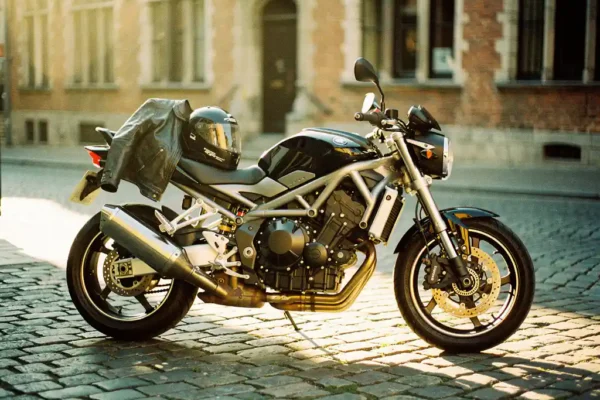 Glanzende motorfiets op Belgische kasseienstraat met leren jas en helm op het zadel, gouden middaglicht.