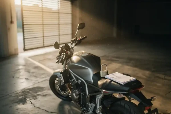 Motorfiets in lege garage met hangslot en verzekeringsdocument op het zadel, gouden licht door halfopen sluiter.