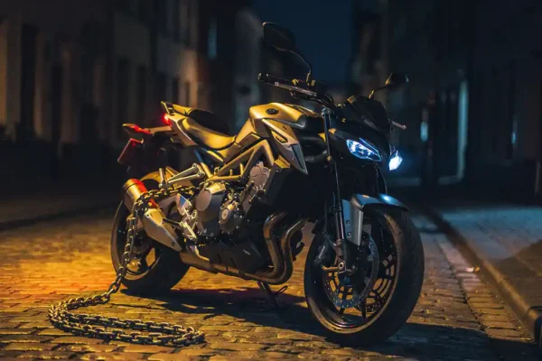 Motorfiets met zwaar kettingslot op achterwiel, geparkeerd op Belgische kasseien bij nacht onder warm oranje straatlantaarn.