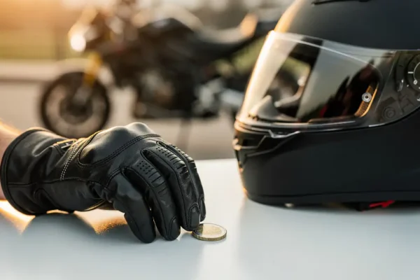 Beglove hand plaatst een euromuntstuk naast een mat zwart motorhelm op wit oppervlak, motor op achtergrond.