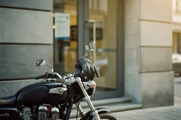 Motorfiets geparkeerd voor een Belgisch verzekeringskantoor, lederen handschoen op het stuur, warm middagzonlicht op chromen details.