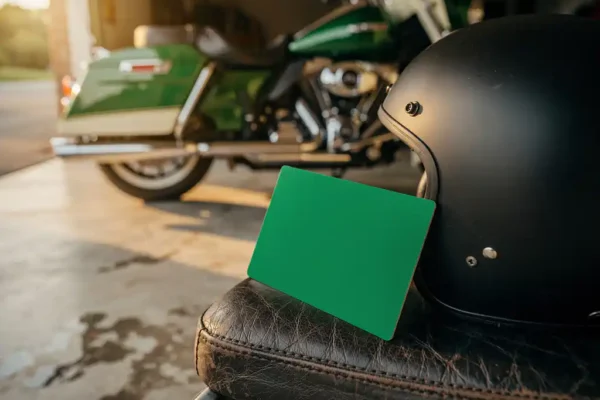Groen verzekeringsbewijs leunend tegen motorhelm op verweerd leren zadel, geparkeerde toermotor vaag op achtergrond.