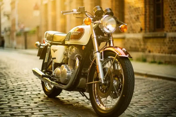 Vintage motorfiets uit de jaren 70 op Belgische kasseienstraat, met glanzend chroom en lederen zadel in gouden middagzon.